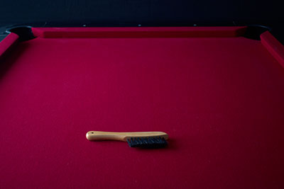 Tan wooden pool table cleaning brush on a red felt billiards table