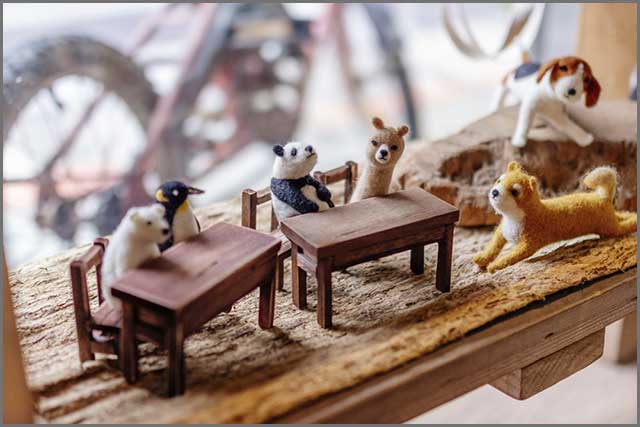 Wild animals made of wool felt gathered around tables