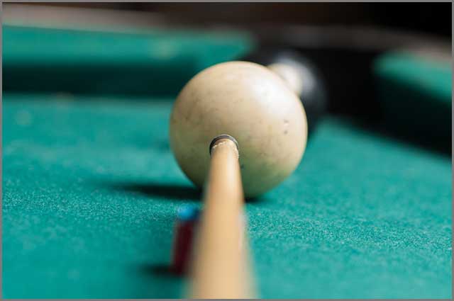 A white billiard ball on a table felt with a cue